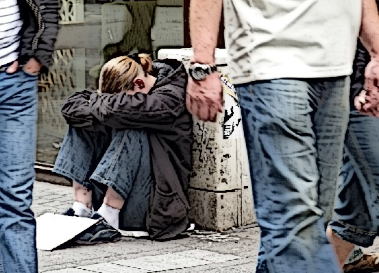A homeless woman sits on the ground with her head down.