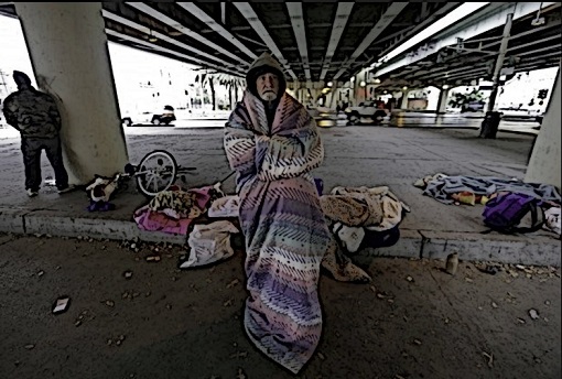 A cold man sits with a blanket wrapped around his body.