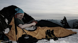 A man is sitting in a small tent on a mountain in snow.
