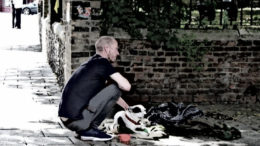 A homeless man kneels near his belongings.