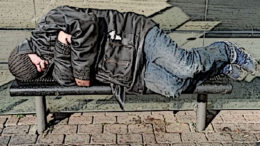 A homeless man sleeps on a bench.